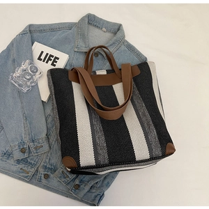 Close-up of striped canvas tote bag with brown leather handles on denim jacket