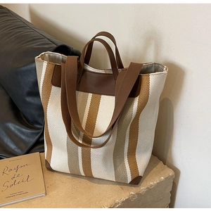 Detailed close-up of striped canvas tote bag with brown leather trim on stone base