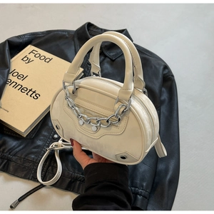 Detail of cream oval handbag with silver rivets, chain decor and metal hardware