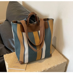 Detailed close-up of striped canvas tote bag with brown faux leather straps and reinforced corners