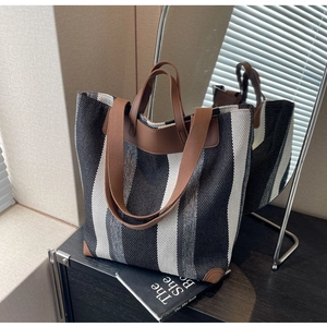 Close-up of striped canvas tote bag with brown leather handles and reinforced base corners
