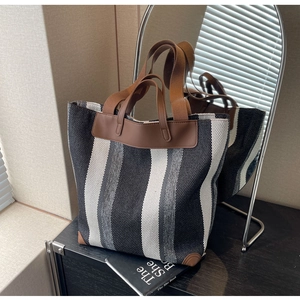 Detail of striped canvas tote bag with brown leather handles and woven texture finish