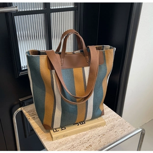 Detail showing dual handles and brown leather trim on a striped canvas tote bag