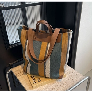 Detail of multi-color striped canvas tote bag with brown leather handles and corner padding
