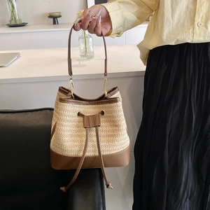 Détail d'un sac seau en paille porté main avec garniture en cuir brun et crochets métal