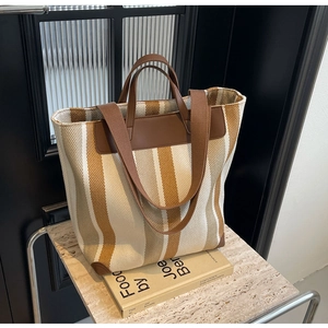 Detail view of striped canvas tote bag with brown leather handles on a display stand