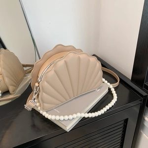 Detailed view of beige shell-shaped bag featuring glossy pearl handle and smooth leather strap