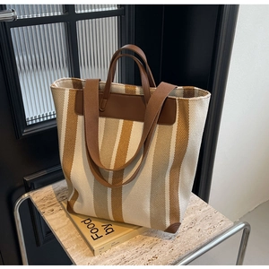 Detail view of large striped canvas tote bag with brown leather handles and corner protectors