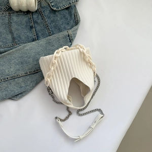 Top view of pleated white bucket bag with resin chain strap and denim jacket