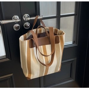 Detail view of canvas tote bag featuring brown vertical stripes and premium leather corners