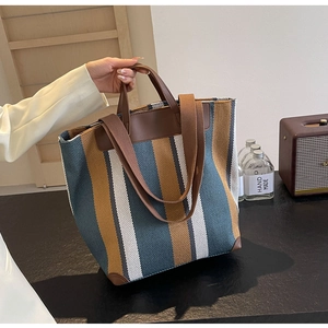 Detail of colorful striped canvas tote bag with brown leather handles and shoulder strap