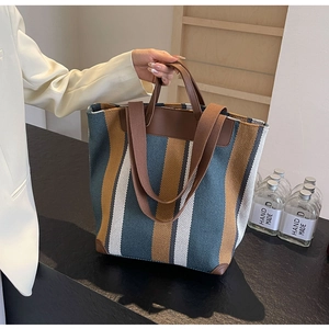 Detail view of canvas tote bag with thick vertical stripes and brown leather handles