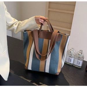 Detail view of large striped canvas tote bag with brown leather handles and wide shoulder strap