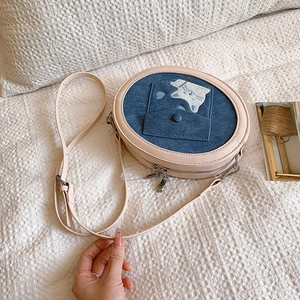 Detail of round denim crossbody bag with cat embroidery and pink leather trim accents
