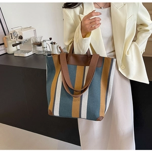 Close-up of a striped woven tote bag with leather straps and reinforced corners in a cafe