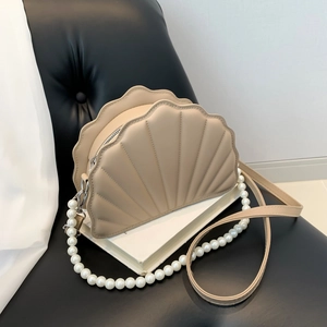 Close-up of shell-shaped crossbody bag with scalloped stitching and pearl chain strap