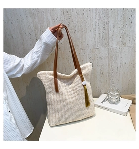 Détail d'un sac cabas en paille tressée avec poignées marron et pompon décoratif vert