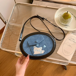 Close-up of small denim crossbody bag with cat embroidery on a stylish striped stand