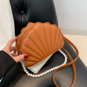Detail of caramel brown shell-shaped crossbody bag featuring quilted texture and pearl chain