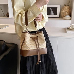 Détail du sac seau en paille tressée avec bordure en cuir marron et boucles dorées