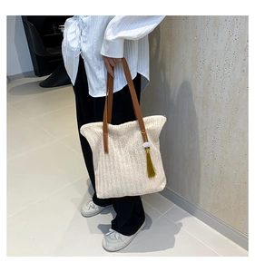 Détail du sac cabas en paille tissée avec bandoulière en cuir brun et pompon doré