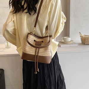Détail du sac seau en paille tressée avec garniture en cuir brun et cordon de serrage