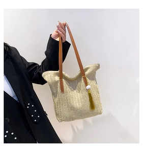 Détail d'un sac seau en paille tissée avec anses en cuir marron et pompon jaune