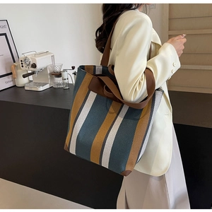 Detail view of the striped canvas tote bag featuring reinforced leather corners and wide straps