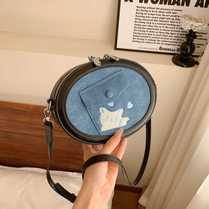 Detailed shot of cat embroidery on a blue denim and black leather crossbody bag