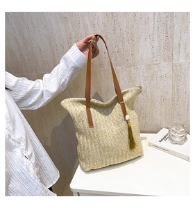 Détail du sac cabas en paille d'été avec anses en cuir marron et pompon vert