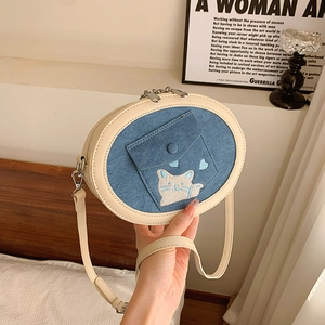 Detail of denim and cream crossbody bag featuring cat embroidery and small pocket