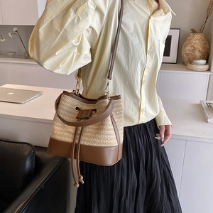 Détail du sac seau en paille tressée avec bordure en cuir marron et boucles dorées chic
