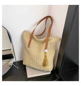 Gros plan détaillé du sac seau en paille avec pompon doré et lanières en cuir
