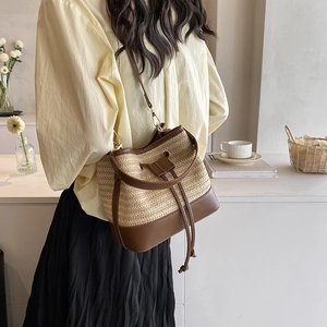 Détail du sac seau en paille tissée avec garniture en cuir et boucles dorées