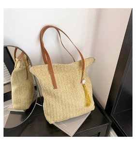 Détail du sac cabas en paille avec anses en cuir marron et pendentif à pompon jaune