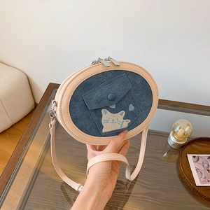 Close-up of denim crossbody bag with cat embroidery and faux leather strap detailing