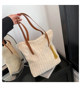 Détails du sac seau en paille beige avec poignées en cuir marron et pompon jaune vif