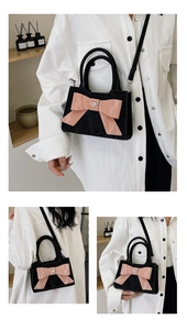 Detail of black pleated crossbody bag featuring a large pink bow and heart ornament