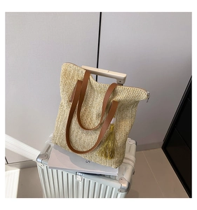 Détail du sac cabas en paille avec anses en cuir marron et pompon doré sur une valise