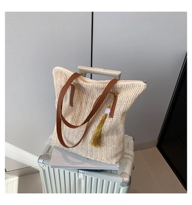 Gros plan détaillé du sac seau en paille avec pompon doré et bandoulière en cuir brun