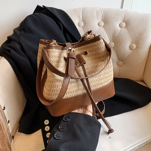 Détail du sac seau en paille tressée avec garniture en cuir brun et boucle dorée
