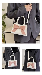 Detail view of white leather tote with pink bow and heart metal charm shown on model