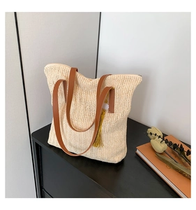 Détail d'un sac cabas en paille tissée avec poignées en cuir marron et pompon jaune