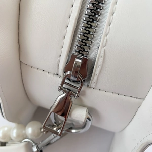 Detail of silver metal zipper and white pearl strap on a minimalist leather shell bag