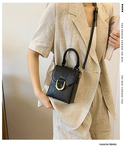 Detail of a black textured mini square bag featuring a gold U-shaped metal buckle