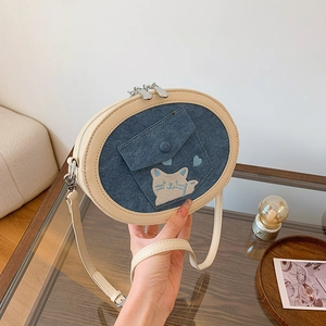 Detail of blue denim oval crossbody bag featuring cat embroidery and beige leather trim