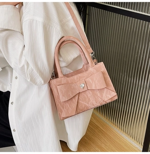 Side view of pink crossbody bag with large bow detail and pleated glossy texture