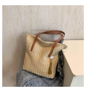 Détail d'un sac en paille avec poignées en cuir marron et breloque décorative à pompon doré