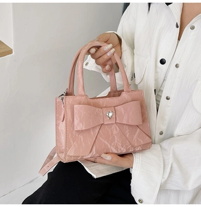 Detailed close-up of pink glossy pleated handbag featuring a large bow and crystal heart
