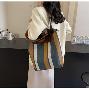 Side view of large striped canvas tote bag with brown leather handles on a model